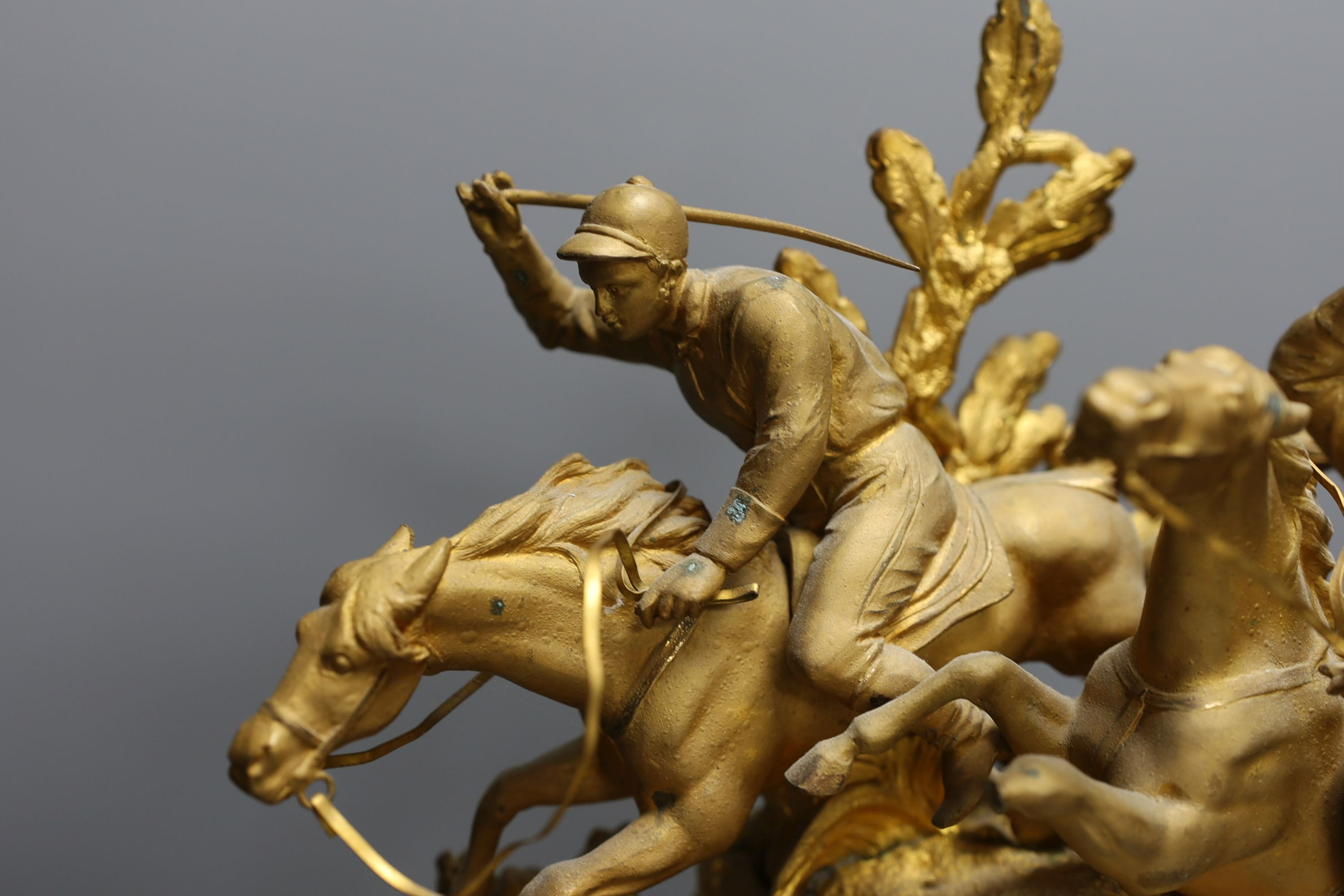 A 19th century gilt spelter mantel clock, having horse and jockey surmount with porcelain panels and circular porcelain dial, on shaped plinth base. 47cm